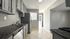 Bright, modern kitchen with sleek grey cabinets, stainless steel appliances, and elegant tile flooring, opening to a sunlit entryway.
