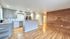 Bright open-plan kitchen and cozy living area featuring sleek gray cabinetry, hardwood floors, and elegant wood-accented wall.