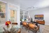 Bright and inviting living room with modern decor, featuring a stylish glass dining table, cozy seating area, and vibrant artwork. Large windows illuminate the space with natural light.