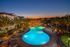 Breathtaking view of a luxurious apartment complex pool surrounded by palm trees, illuminated by warm evening lights, creating a resort-style ambiance at sunset.