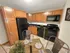 Apartment kitchen with wood cabinetry, black appliances, and tile flooring at Woodlands at Nashua