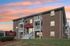 Exterior view of Hamilton Park in Methuen, Massachusetts showcasing the leasing office and apartment homes within the same brick building, complete with private balconies, a welcoming entrance, and community signage at sunset