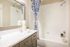Renovated bathroom with shaker style neutral cabinets with pulls, quartz cabinets and framed mirror
