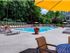The Henry Apartments, exterior, sparkling blue pool, gray lounge chairs, yellow umbrella at gray table, trees,
