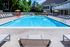 The Henry Apartments, exterior, sparkling blue pool, gray lounge chairs, yellow umbrella at gray table, trees, building exterior, balcony