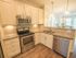 Kitchen with stainless steel appliances, pendant lighting, granite countertops, white cabinetry and nickel fixtures looking into living room