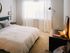 The Henry Apartments, interior, bedroom, white bed, tan carpet, large window, dark dresser