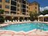 Exterior view of a shimmering pool surrounded by lounging chairs | A building boarded with palm trees can be seen in the background |  Mirasol at Celebration