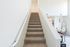 Warmly lit carpeted staircase leading to an inviting living space with contemporary decor.