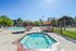 Sparkling swimming pool with adjacent hot tub, surrounded by sun loungers and umbrellas under a clear blue sky.