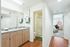 Bright bathroom with dual sinks, wood cabinetry, and a hallway leading to a cozy bedroom.