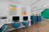 Modern communal workspace with sleek blue chairs, vibrant artwork, and natural light, ideal for productivity.