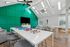 Vibrant communal lounge featuring modern seating, a large TV, and game boards for recreation, enhanced by natural lighting and a bold green accent wall.