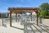 Inviting outdoor patio with elegant wooden pergola, overlooking a sparkling pool and surrounded by lush greenery, ideal for relaxation and gatherings.