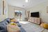 Bright and inviting living room with modern decor, a plush gray sofa, and a large TV, leading to a sunlit patio through sliding glass doors.