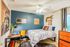 Charming bedroom with cozy decor, featuring a blue accent wall, stylish desk, and vibrant artwork for a welcoming ambiance.