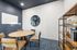 Modern meeting room with stylish wooden round table, four plush chairs, and a chic open bookshelf. The room features a sleek navy accent wall, elegant lighting, and a large circular mirror creating a spacious feel.
