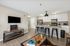 Modern open-concept living room with sleek kitchen, stylish bar stools, and wall-mounted TV in a contemporary apartment.