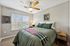 Cozy bedroom with a stylish bed, vibrant pillows, and a ceiling fan, illuminated by natural light through large windows.