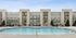 Elegant apartment complex featuring a pristine swimming pool, surrounded by stylish lounge chairs and shaded seating, perfect for relaxation and leisure.