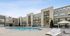 Modern apartment complex featuring a resort-style swimming pool, sun loungers, and private balconies under a clear blue sky.
