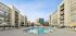 Luxurious apartment complex with inviting outdoor pool, surrounded by modern multi-story buildings under a clear blue sky.