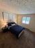 Cozy bedroom with stylish decor, featuring a comfortable bed, elegant wall art, natural light from large window, and plush carpeting.