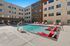 Modern apartment complex courtyard showcasing a sparkling swimming pool with stylish red lounge chairs and sunlit seating areas.