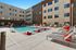 Modern apartment complex courtyard featuring a sparkling swimming pool, vibrant red sun loungers, and stylish poolside seating, perfect for relaxation and leisure.