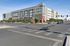 Modern apartment building exterior in a vibrant urban setting at a bustling intersection, surrounded by lush greenery and wide streets.