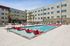 Modern apartment complex featuring a beautiful outdoor pool with stylish red lounge chairs and palm trees, perfect for relaxation.