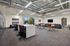 Modern office space with open seating, sleek bar stools, plush sofas, and vibrant artwork, illuminated by natural light.