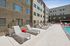 Modern apartment complex with sunlit outdoor pool area, stylish lounge chairs, and vibrant red accents.