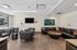 Modern lounge area with stylish gray chairs, a black sectional sofa, contemporary artwork, and a sleek wooden coffee table, filled with natural light from large windows.