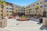 Bright courtyard of a modern apartment complex featuring palm trees, seating areas, and stylish architecture.