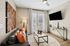 Modern living area featuring a sleek leather sofa with vibrant cushions, contemporary art, and a wall-mounted TV, complemented by abundant natural light from large French doors.