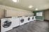 Modern laundry room with a row of state-of-the-art washers and dryers, featuring sleek wood flooring and vibrant lighting for a clean and convenient laundry experience.