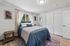 Inviting bedroom with stylish decor, featuring a cozy bed with blue accents, elegant artwork, and natural light through the window.