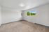 Bright and airy room with plush carpets and a large window overlooking lush greenery, offering a serene atmosphere.