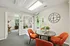 Elegant office space with a modern round table and vibrant orange chairs, featuring a large decorative wall clock and abundant natural light.