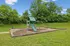Charming play area featuring a modern swing set and slide surrounded by lush green trees and open grassy space, perfect for fun outdoor activities.