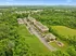Scenic aerial view of a charming apartment complex nestled amidst lush greenery and rolling hills, featuring ample parking and a serene playground for family enjoyment.