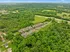 Aerial view of charming apartment complex surrounded by lush green forest, offering both tranquility and easy access to nearby roads.