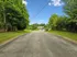 Serene suburban street lined with lush green trees, leading to a distant apartment complex under a clear blue sky.