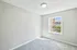 Bright, unfurnished room with soft gray carpet and a large window offering a sunny, inviting outdoor view.