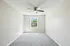 Bright and inviting room with soft gray carpeting, a window offering scenic views, and a ceiling fan for comfort.