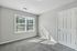 Bright bedroom with plush gray carpeting, large window allowing natural light, and a white closet door.