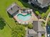 Aerial view of a charming residential community featuring a kidney-shaped pool with lounge chairs and umbrellas, surrounded by lush greenery and well-maintained paths.