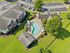 Bird's-eye view of a luxurious apartment community featuring a stylish kidney-shaped pool, surrounded by lush green lawns and ample parking space.