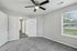 Bright and airy bedroom with fresh gray carpeting, modern ceiling fan, and large window showcasing lush greenery.